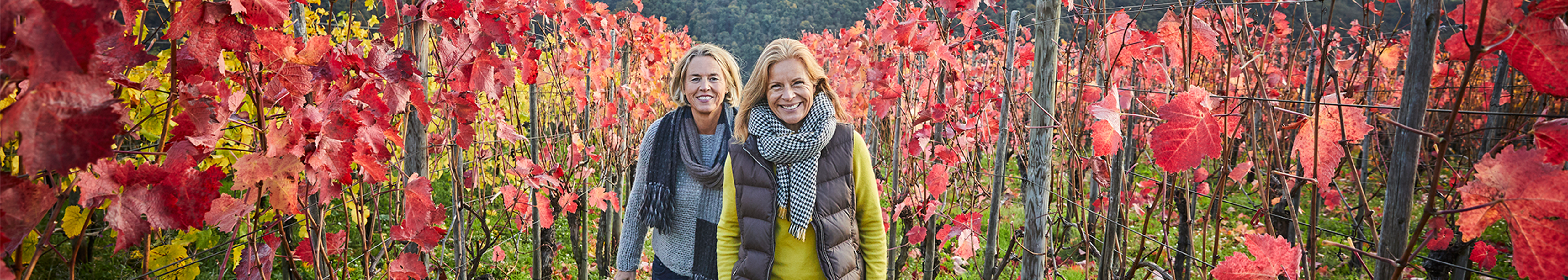 Two smiling women in their 50s who are eligible for a free mammogram, walking through a vineyard